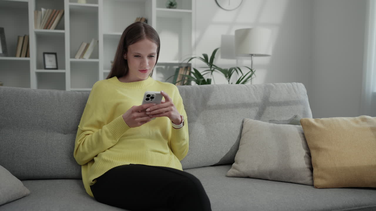 A woman is sitting on a couch and using her phone