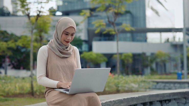 Woman in hijab working on laptop outdoors