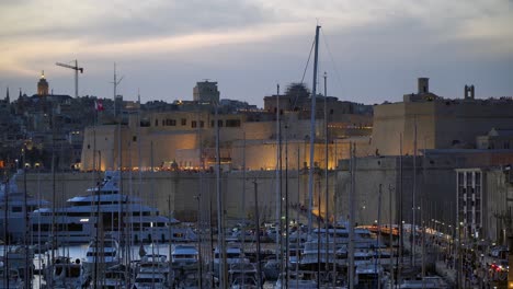 distant view of fort st angelo, decorated with candles through the masts of ships on the waterfront during early evening in birgu, malta.