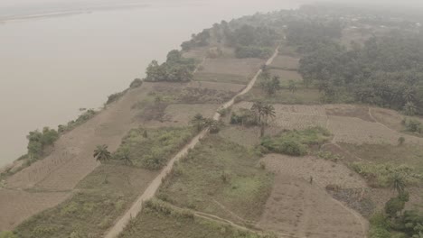 Aerial-shot-of-coastal-farmland-near-River-Niger-revealing-a-narrow-road-to-the-community