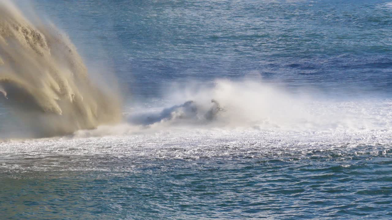A powerful dredging operation pumps sand into the ocean, creating dramatic splashes and waves under bright daylight