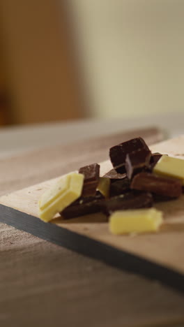 vertical video of person putting chunks of milk plain and white chocolate onto chopping board