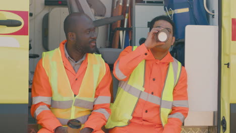 two medical assistances drinking coffee and talking on the ambulance