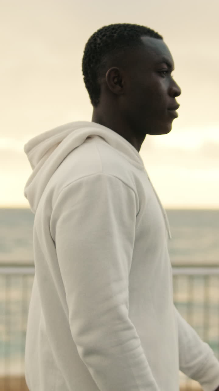 Thoughtful Young Man in White Hoodie Walking by the Ocean