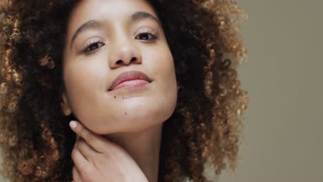 Biracial-woman-with-dark-hair-touching-neck-on-beige-background,-slow-motion