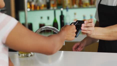 una mujer de raza mixta celebrando el día de san patricio pagando por cervezas en un bar.