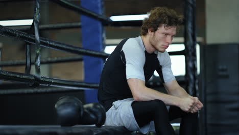 Worried-fighter-waiting-for-fight-in-fitness-center.-Kickboxer-sitting-at-gym