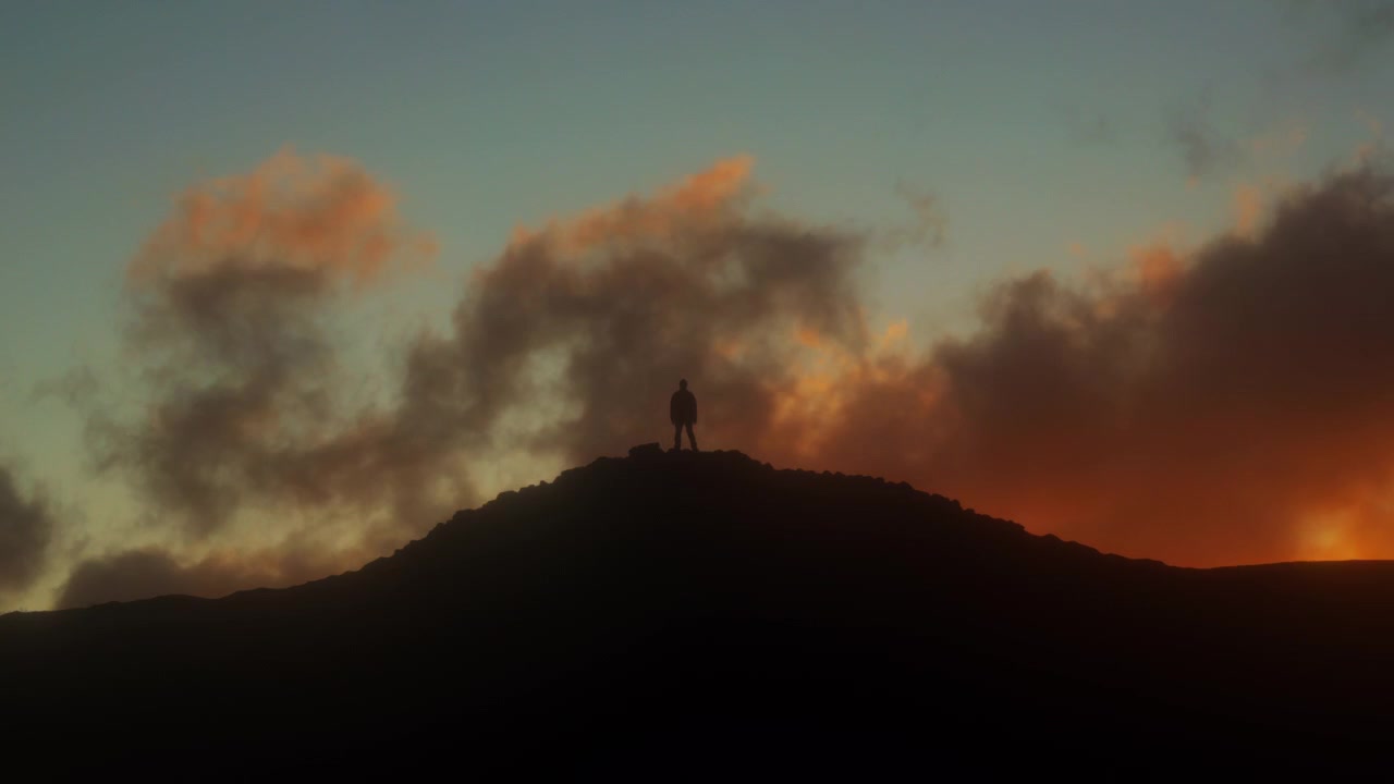 Figura masculina silueteada de pie observando las nubes del atardecer pasar, creando una sensación de asombro y aventura