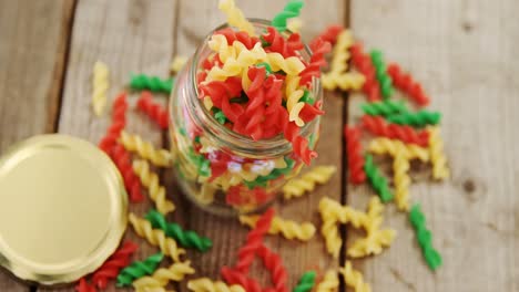 Various-colored-gemelli-pasta-overflowed-of-the-jar-on-the-wooden-background