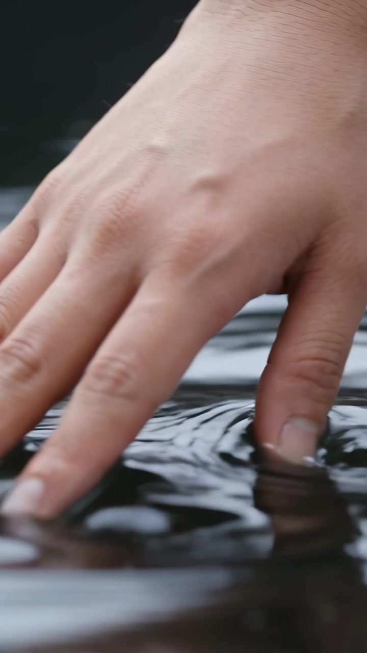 Vertical video: Touching water, single hand creating ripples on dark pool to observe reflection