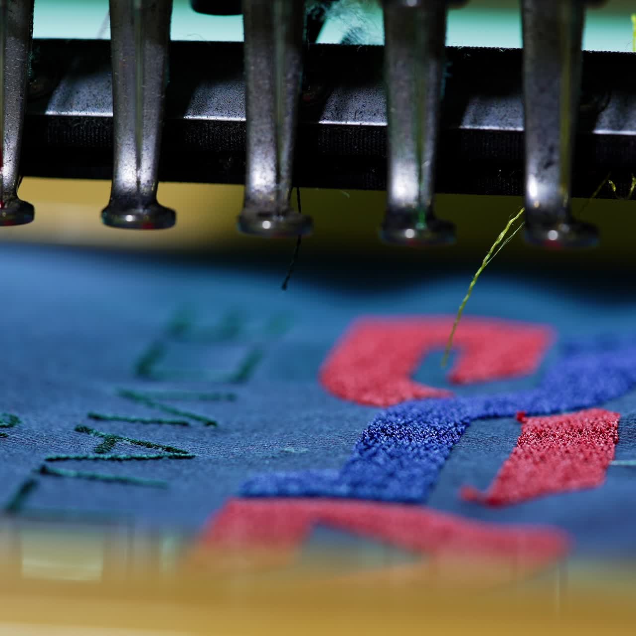 Dressmaking machine making a thread stitches. Work of automated embroidery machine on blue cloth. Sewing needle moving rapidly on fabric. Close-up