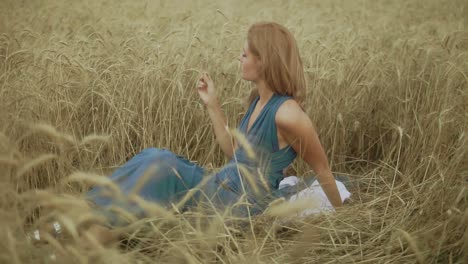 attractive young woman sitting in the golden wheat field. her hand is touching wheat ears. harvest concept. harvesting. slow