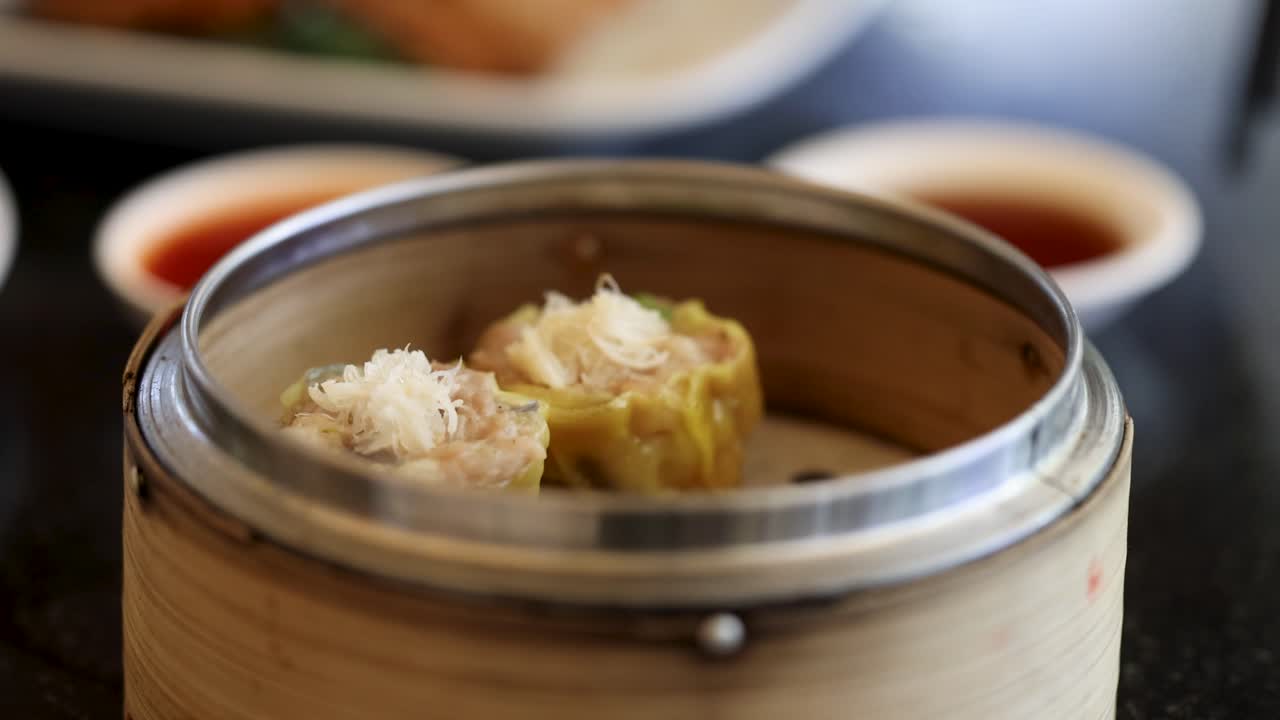 Tampilan dekat dim sum yang mengepul dalam keranjang bambu, menyoroti makanan jalanan tradisional Asia dalam suasana yang semarak