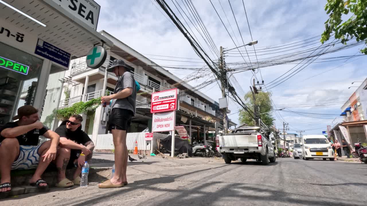 Wide-angle timelapse of tropical Phuket street with vehicles, pedestrians, shops, and bright daylight