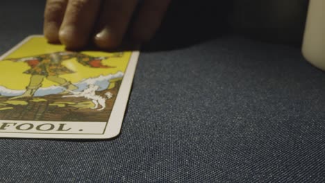 close up shot of person giving tarot card reading laying down the fool card on table