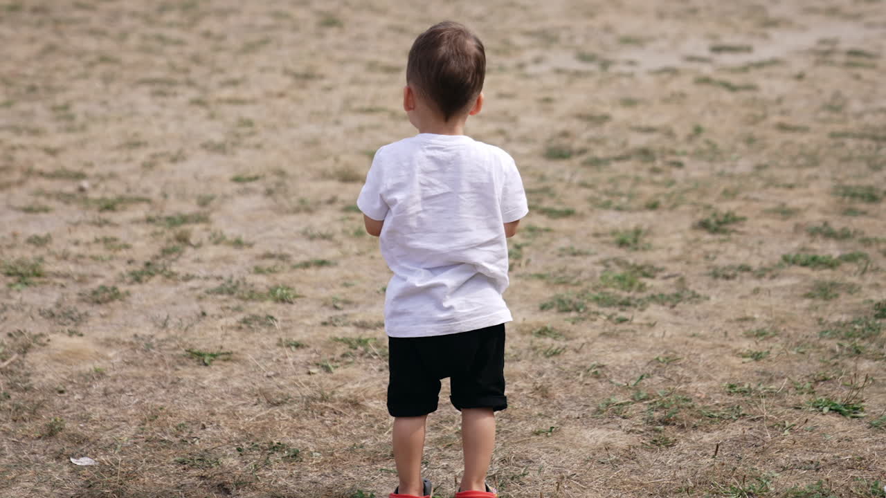 Rear view of a little kid standing at the beach. Cute kid turns around and starts to hop cheerfully.