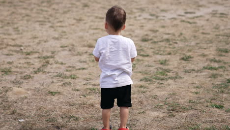 rear view of a little kid standing at the beach. cute kid turns around and starts to hop cheerfully.