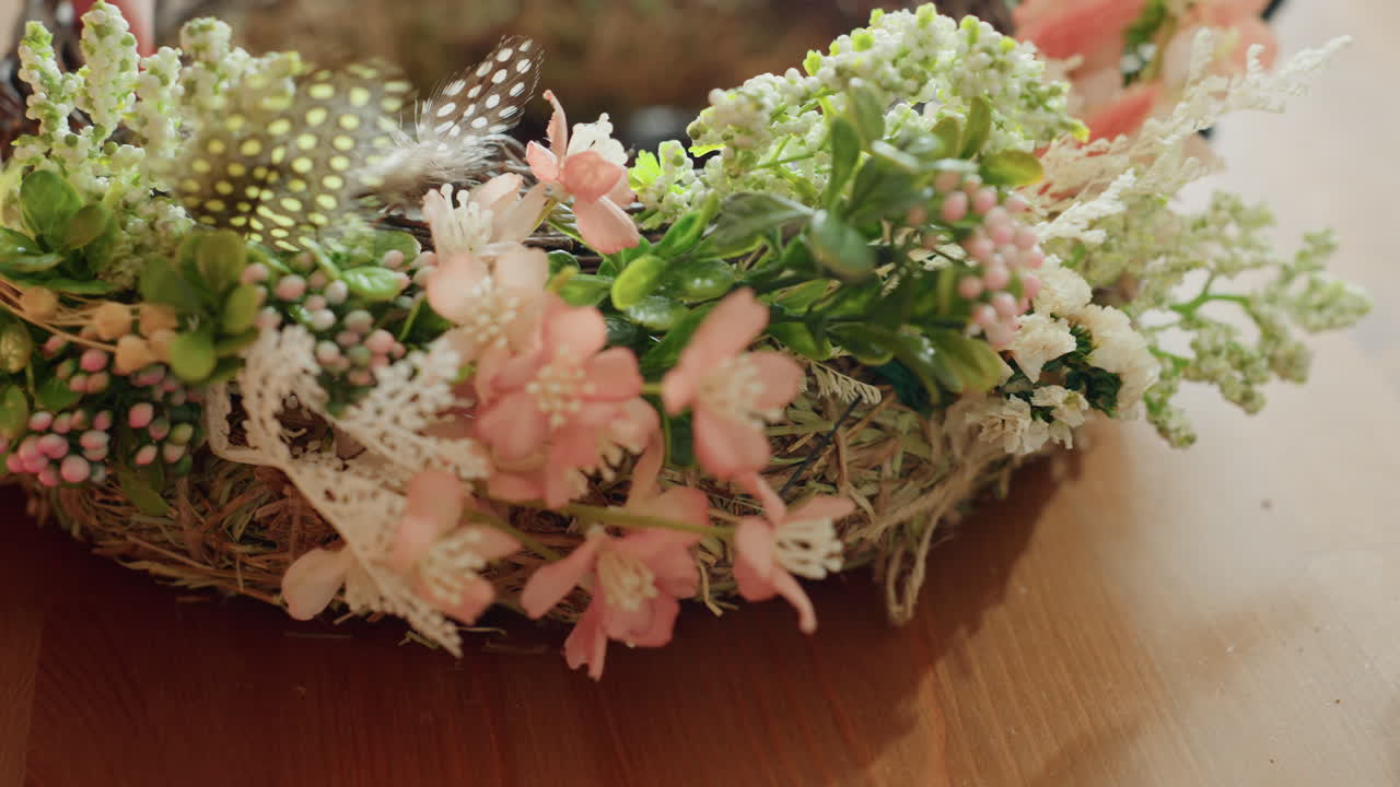 Closeup of hands adjusting rustic wreath made of hay and twigs with floral accents on wooden table, green moss decor placed on tree slices creating natural arrangement for seasonal craft project indoors