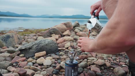 hiker pouring coffee from portable coffee maker by the lake of anderdalen national park in senja island, norway with mountains in the background