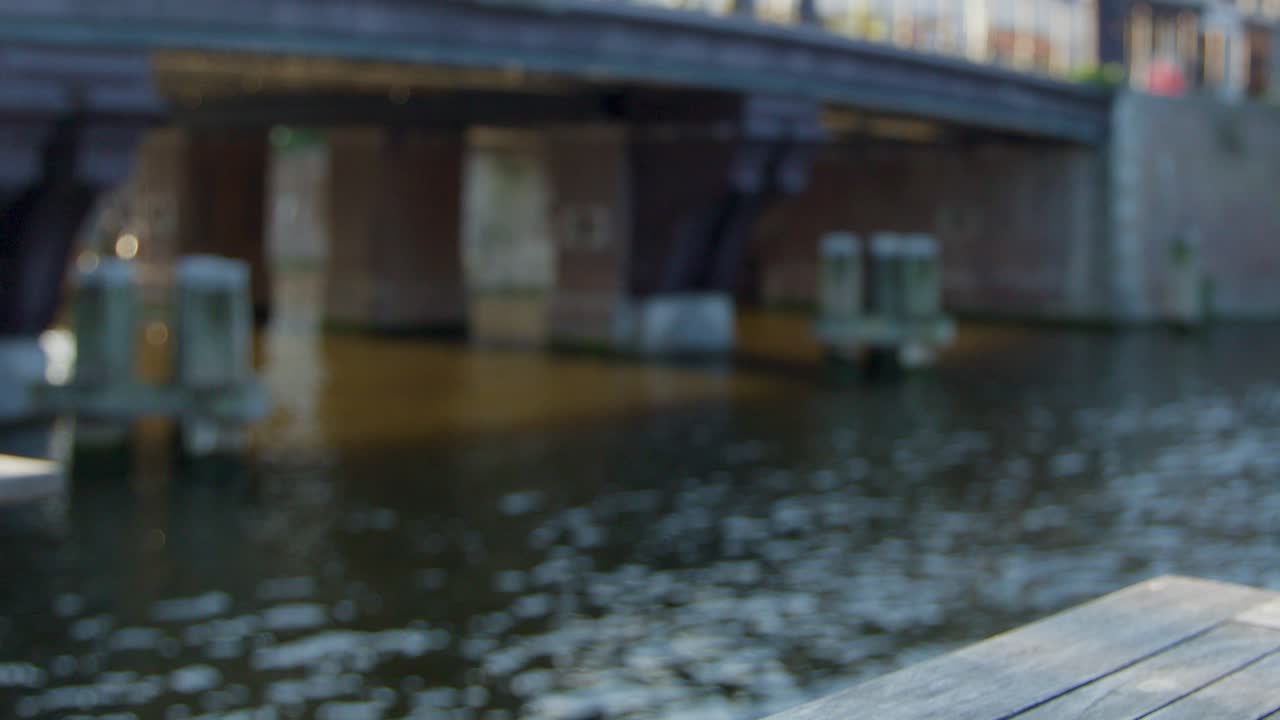 Hand sets glass of beer on wooden table by canal in Haarlem, Netherlands, daylight
