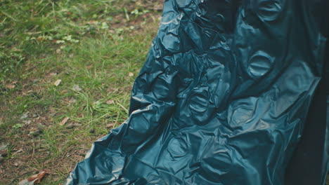 Close up of crinkled tent fabric as it is being opened on grassy ground with blurred surroundings, showing material texture and outdoor setup action in natural forest environment