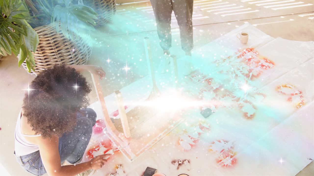 Seated crafter adjusting frame, arranging dyes on cloth for craft, teal overlay sweeping over cloth