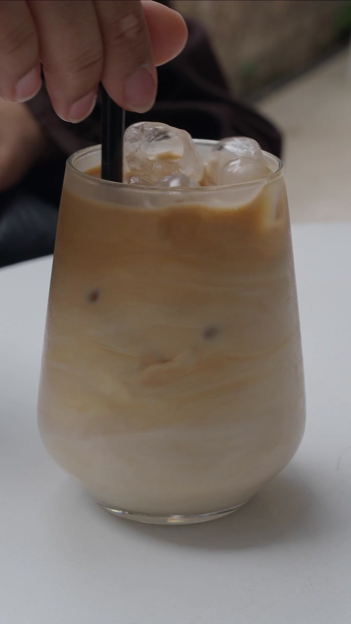 Hand Stirring a Refreshing Iced Latte with Ice Cubes
