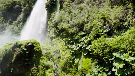 pan left of salto el leon waterfall spraying water over rocks covered with moss in green rainforest near pucon, chile