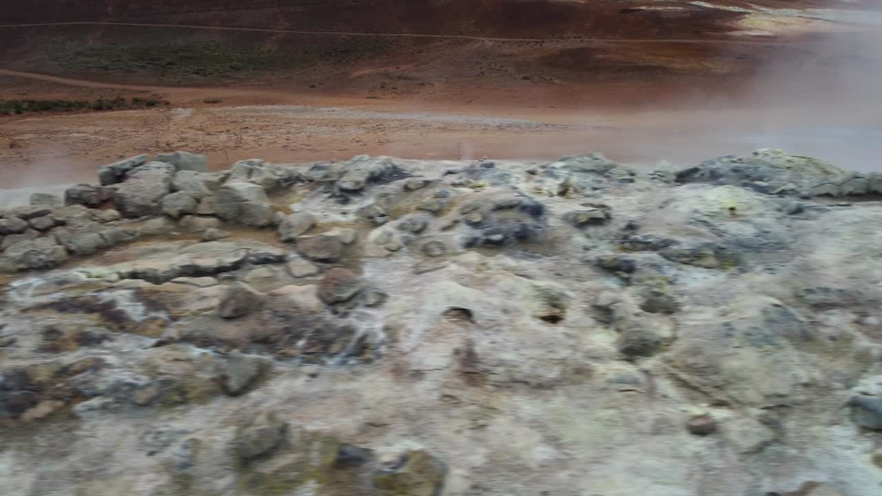 Vista drone che mostra un terreno geotermico fumante con depositi minerali gorgoglianti e un terreno ricco di zolfo, creando un drammatico paesaggio vulcanico in Islanda.