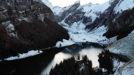 Aerial-flyover-up-away-from-Seealpsee-in-Appenzell,-Switzerland-in-winter-with-a-reflection-on-the-lake---4k