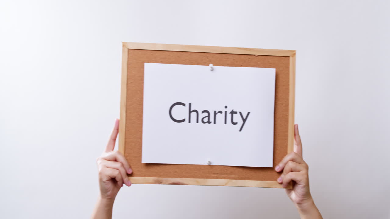 여자의 손은 복사 공간이 있는 흰색 스튜디오 배경에 자선이라는 단어가 적힌 종이를 보여줍니다.