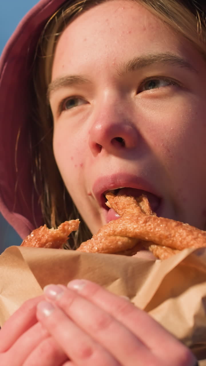 primer plano de una mujer disfrutando de un bocadillo con la luz iluminada destacando su cara en un entorno urbano de invierno, parque al aire libre nevado en el fondo
