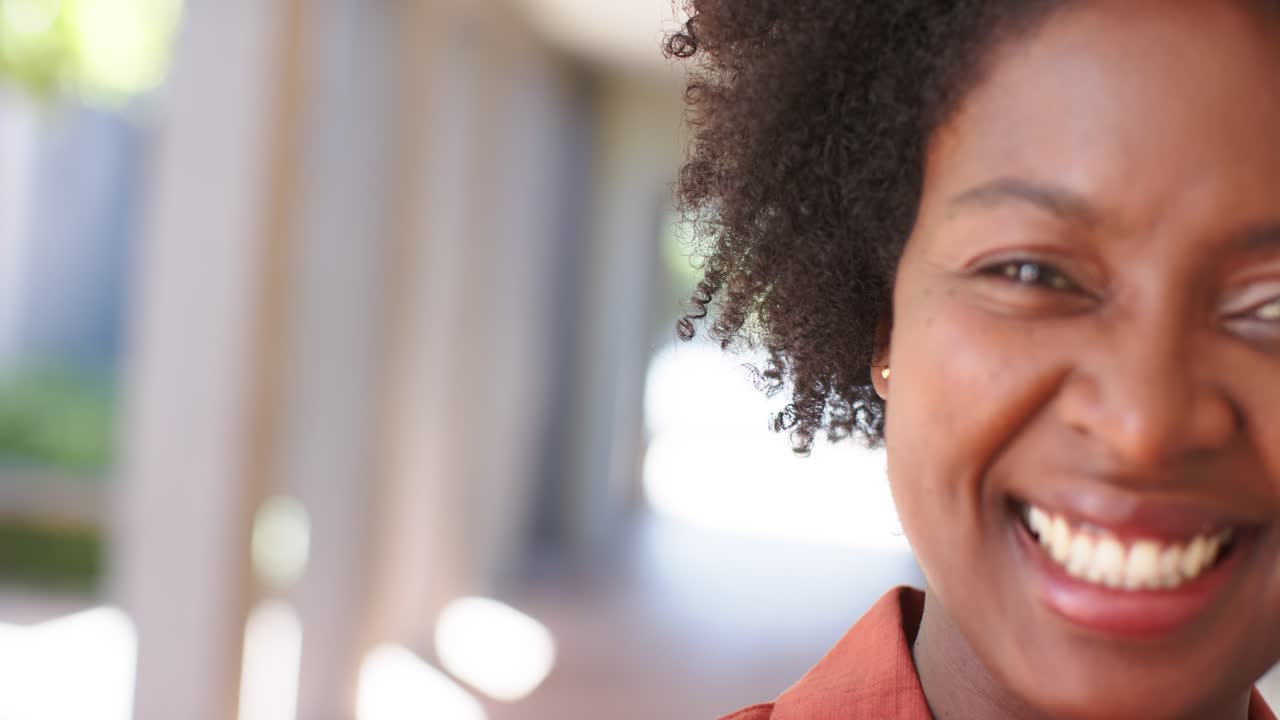 Adult African American woman hearing offscreen voice, smiling, laughing in hall in rust top, studs