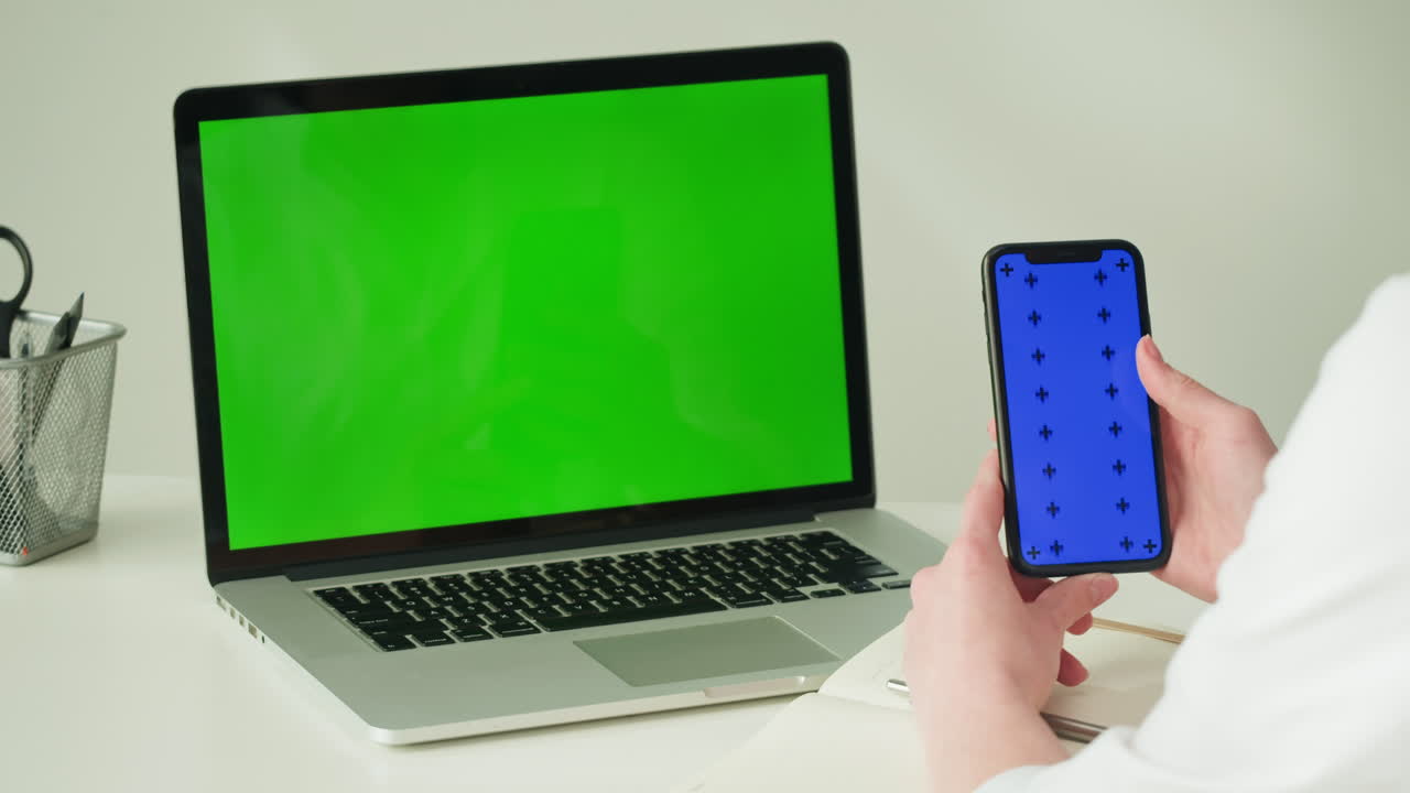 Person using laptop and smartphone with green and blue screens