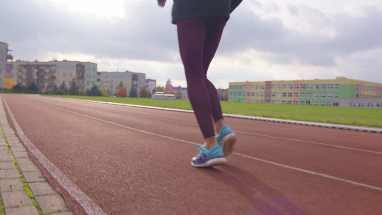 vista baja de las piernas de una joven deportista corriendo en cámara lenta en una pista atlética mientras los rayos del sol se reflejan