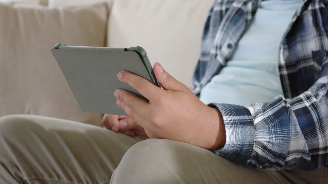 Male on sofa starting cradling tablet with grey cover, tapping, swiping focusing on screen