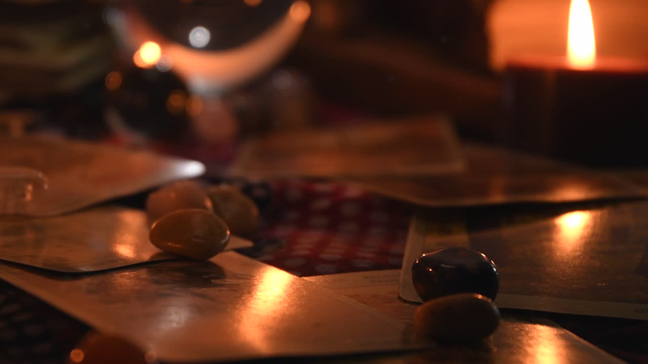 fondo de una mesa de adivinos cubierta de tela, con bolas de cristal, piedras, fósforos, cartas, libros antiguos y velas con llamas parpadeantes