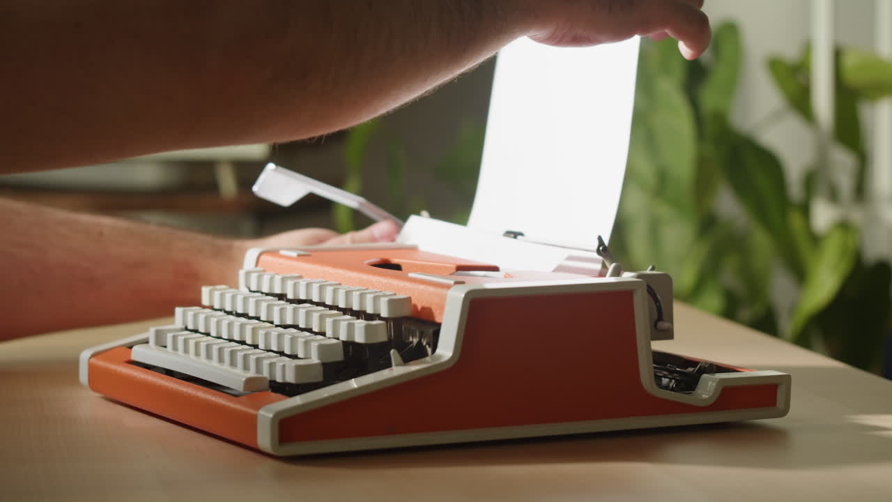 Persona che inserisce un foglio e digita su una macchina da scrivere vintage arancione