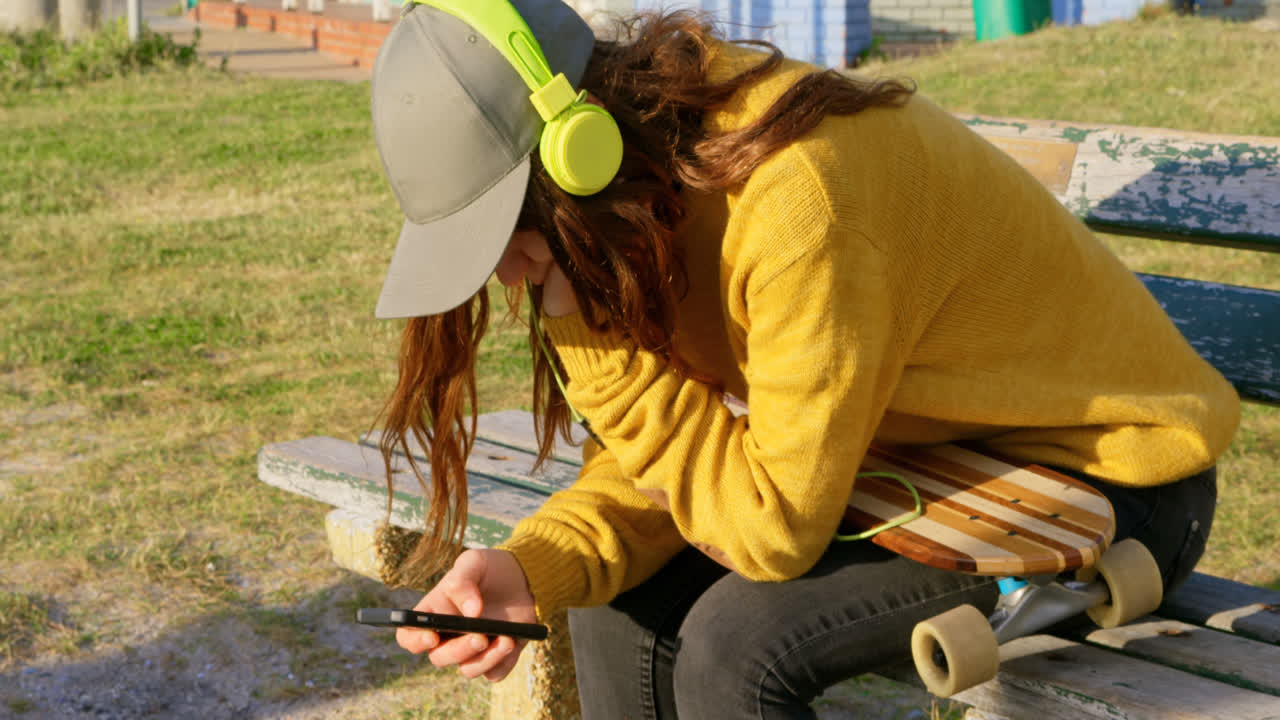 Vista lateral de jovem mulher caucasiana ouvindo música e usando o celular na praia 4k