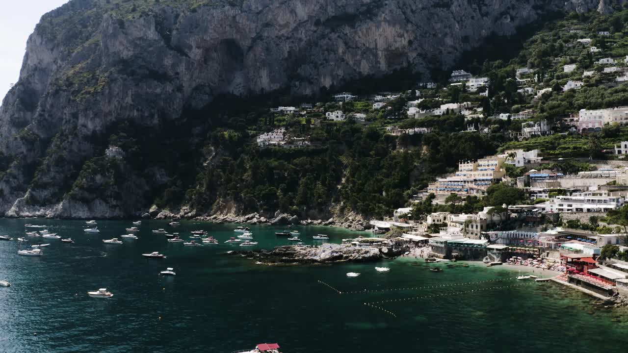 Wide drone shot of the water off Capri, Italy's coast with buildings lining the shore