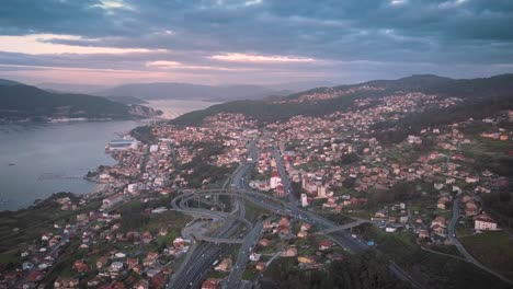 Vista-Aérea-De-La-Autopista-Ap9-Al-Atardecer-Colorido-En-El-Tráfico-Nocturno-Y-El-Puente-Colgante-Sobre-El-Océano-Atlántico-En-Vigo,-España