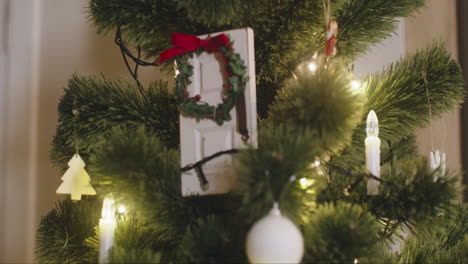 camera focuses on white door decorated with christmas wreath hanging on christmas tree with lights