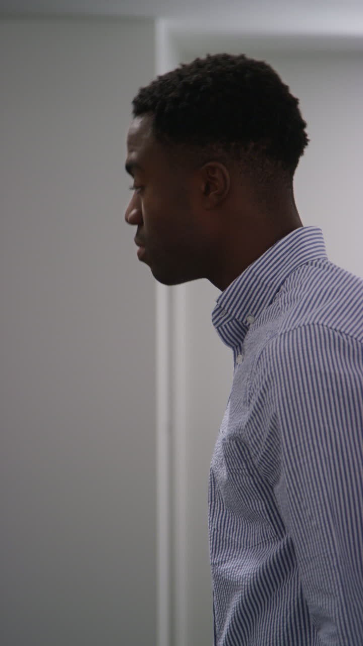Vertical Video Of Young Man With Mental Health Issues Standing Leaning Against Wall In Office Looking Depressed And Unhappy