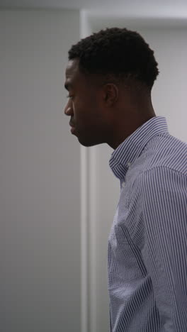 vertical video of young man with mental health issues standing leaning against wall in office looking depressed and unhappy