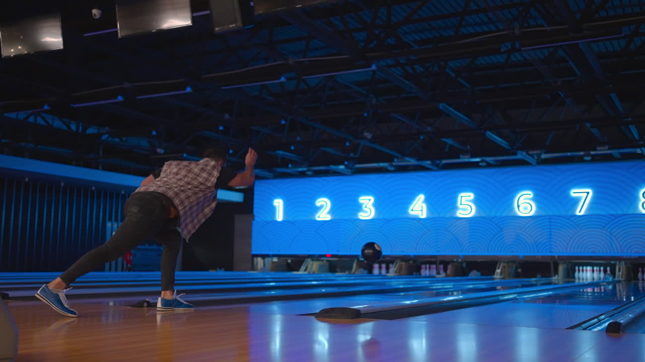 Caucasian Man in bowling throws a ball in slow motion and knocks down skittles. Play bowling. Throw balls on the floor of the bowling club