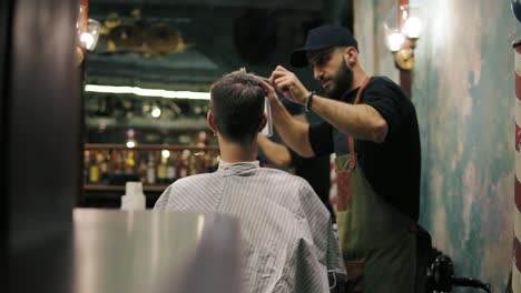 Bearded-hairdresser-spraying-water-and-combing-wet-hair-of-his-male-client-in-a-retro-stylish-barber-shot.-Male-hairstyle