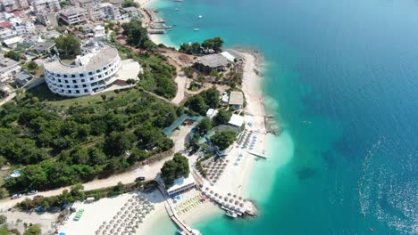 Vista-De-Drones-En-Albania-Volando-Sobre-Playas-De-Arena-Blanca,-Aguas-Azules-Cristalinas,-Pequeñas-Islas-Verdes,-Barcos-Y-Hoteles,-Día-Soleado-En-Ksamil