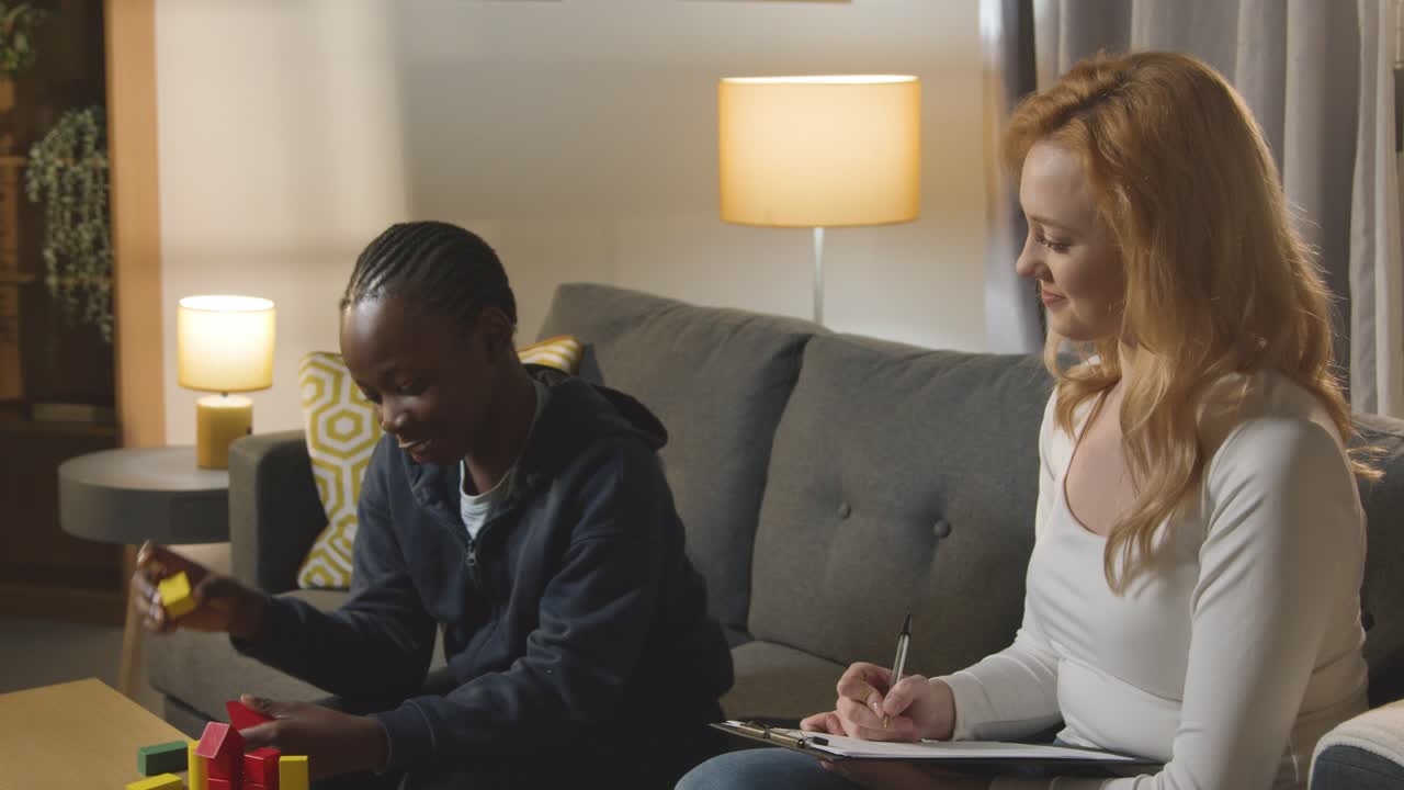 Boy On ASD Spectrum Being Helped Or Assessed By Female Teacher Or Educational Psychologist At Home