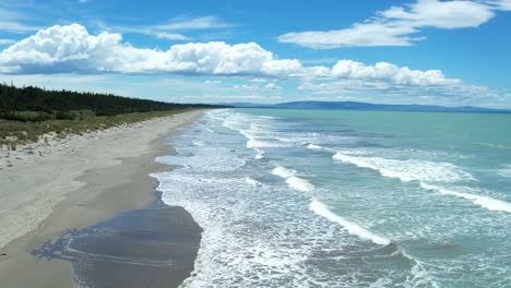 Low-aerial-across-beautiful-rolling-waves-in-summertime---Woodend-Beach,-Pegasus-Bay