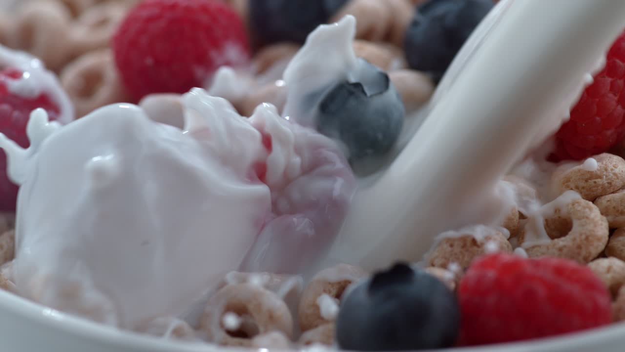 Leite derramando em tigela de cereal e frutas vermelhas.